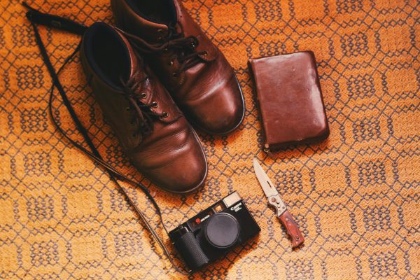 Brown leather shoes, a vintage camera, knife and wallet on a patterned background.