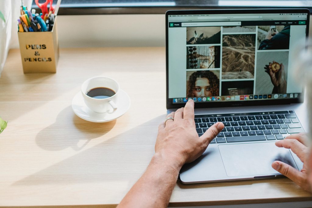 Crop anonymous male searching photos on internet using netbook while drinking coffee at table